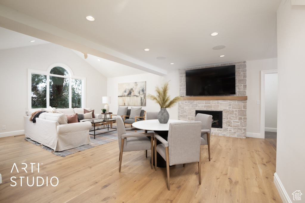 Dining room featuring vaulted ceiling with beams, a stone fireplace, and light hardwood / wood-style floors