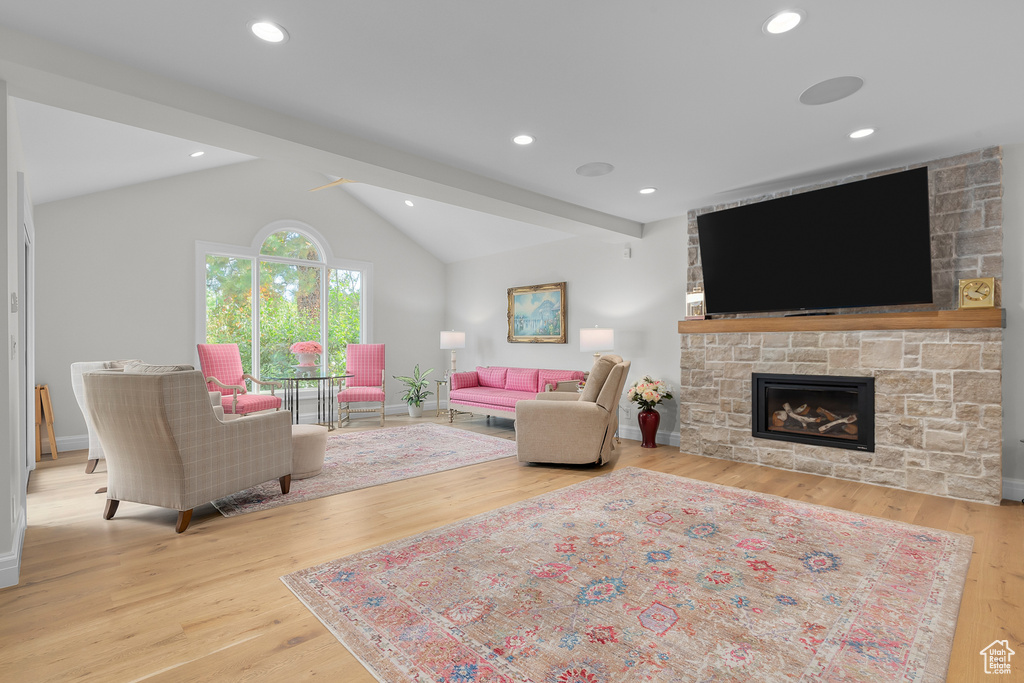 Living room with vaulted ceiling, a fireplace, and light hardwood / wood-style floors