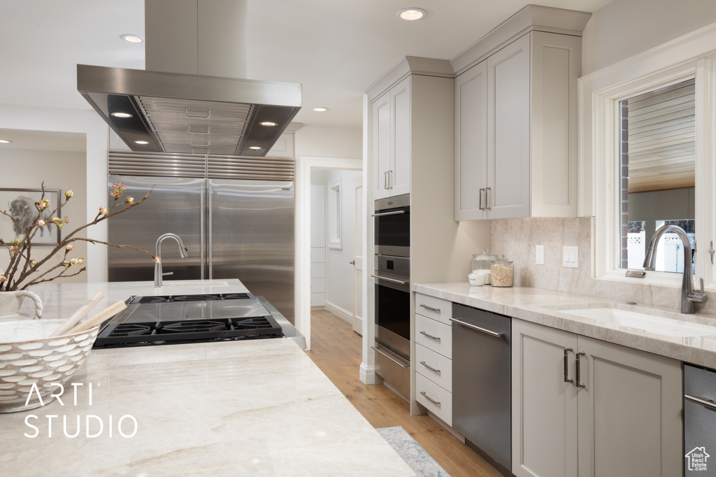 Kitchen with sink, light stone counters, island exhaust hood, stainless steel appliances, and white cabinets