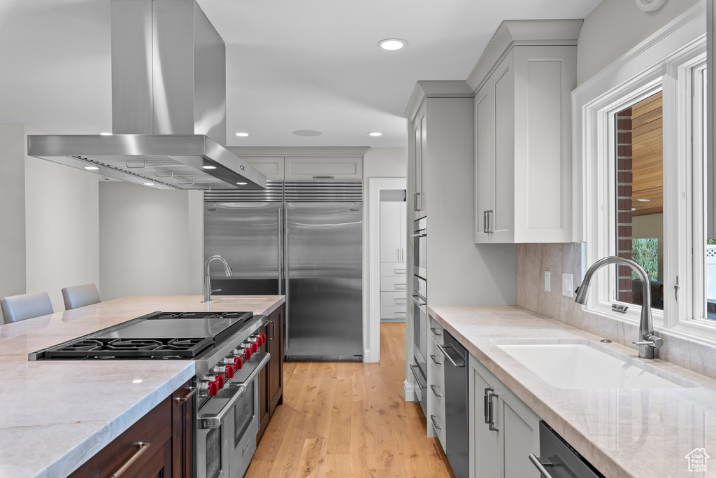 Kitchen with wall chimney range hood, a kitchen breakfast bar, light hardwood / wood-style floors, sink, and premium appliances