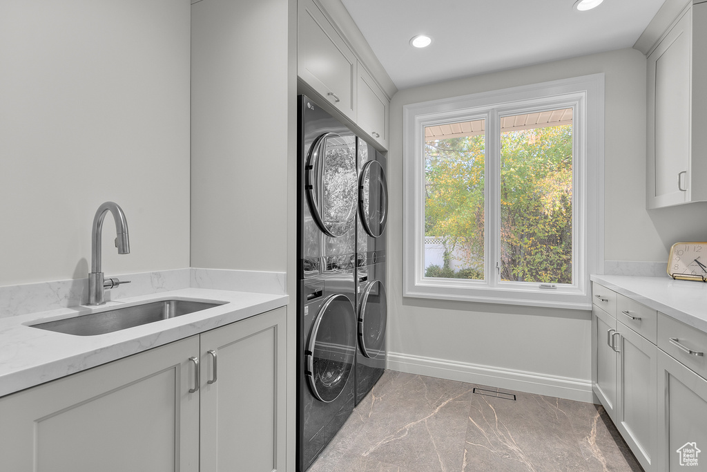 Washroom with sink, cabinets, and stacked washer and clothes dryer