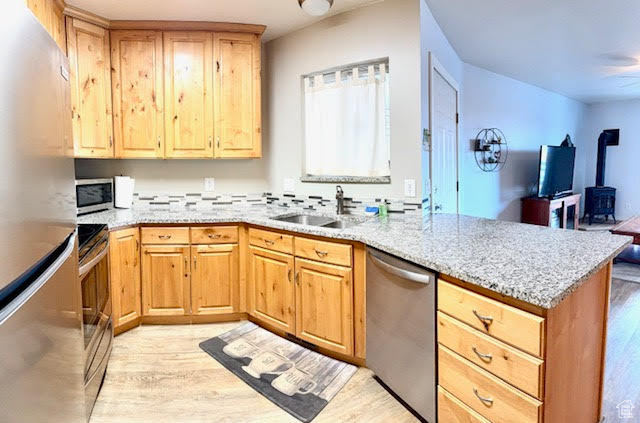 Kitchen featuring light hardwood / wood-style flooring, kitchen peninsula, sink, light stone countertops, and appliances with stainless steel finishes