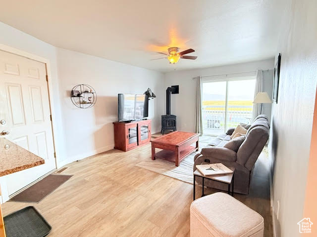 Living room with hardwood / wood-style floors, a wood stove, and ceiling fan