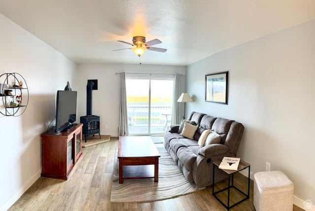 Living room with a wood stove, light wood-type flooring, and ceiling fan