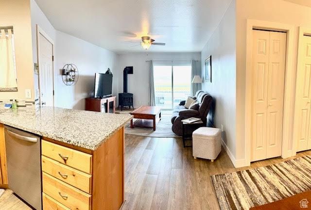 Living room with ceiling fan, a wood stove, and light wood-type flooring