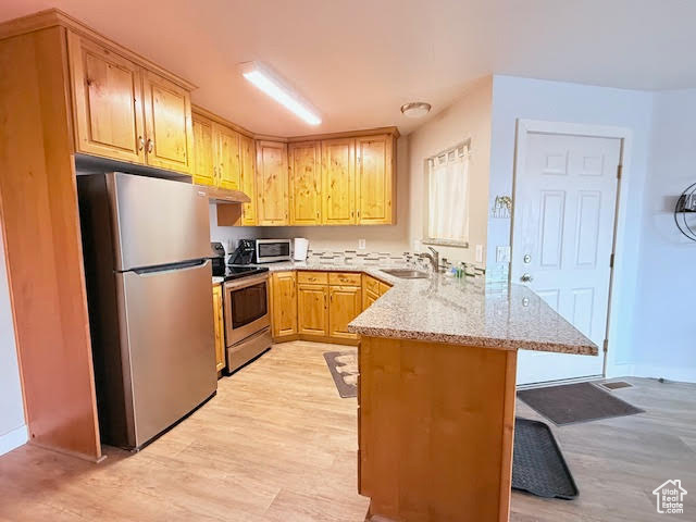 Kitchen featuring light stone countertops, appliances with stainless steel finishes, sink, light wood-type flooring, and kitchen peninsula