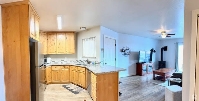 Kitchen featuring light brown cabinets, a wood stove, light wood-type flooring, appliances with stainless steel finishes, and ceiling fan