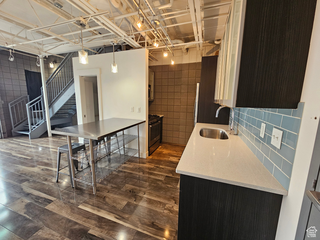 Kitchen with sink, gas stove, tile walls, decorative light fixtures, and dark wood-type flooring