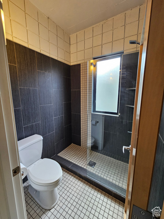 Bathroom with toilet, tiled shower, tile walls, and tile patterned flooring