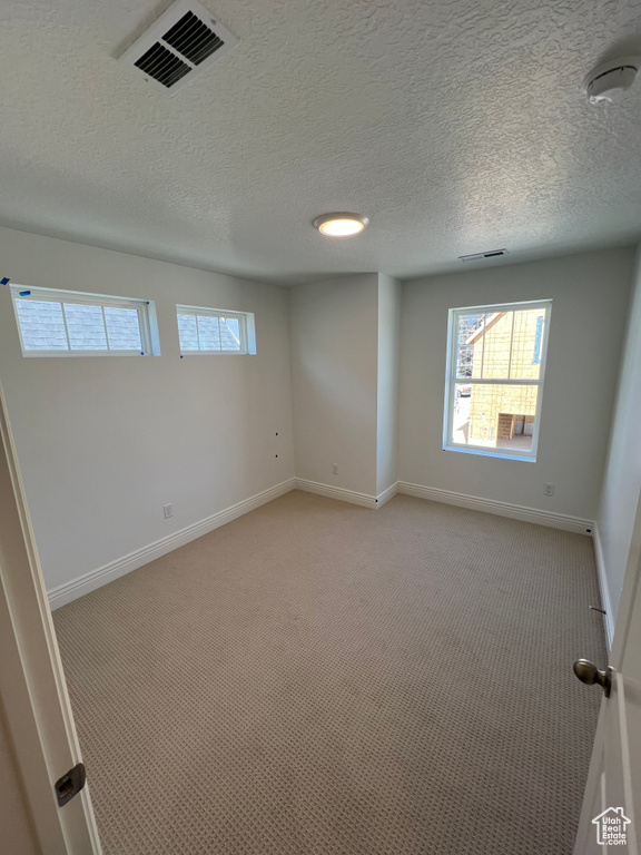 Spare room featuring light carpet, baseboards, visible vents, and a wealth of natural light