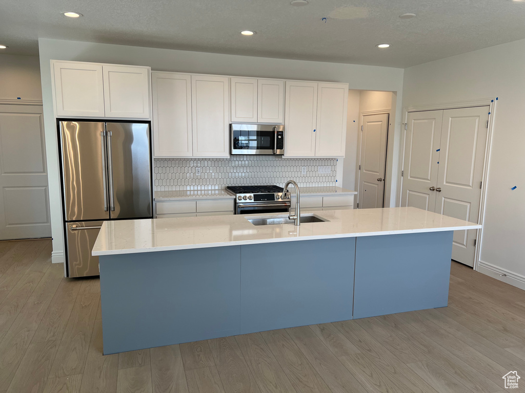Kitchen featuring light wood-style flooring, white cabinetry, backsplash, appliances with stainless steel finishes, and a sink