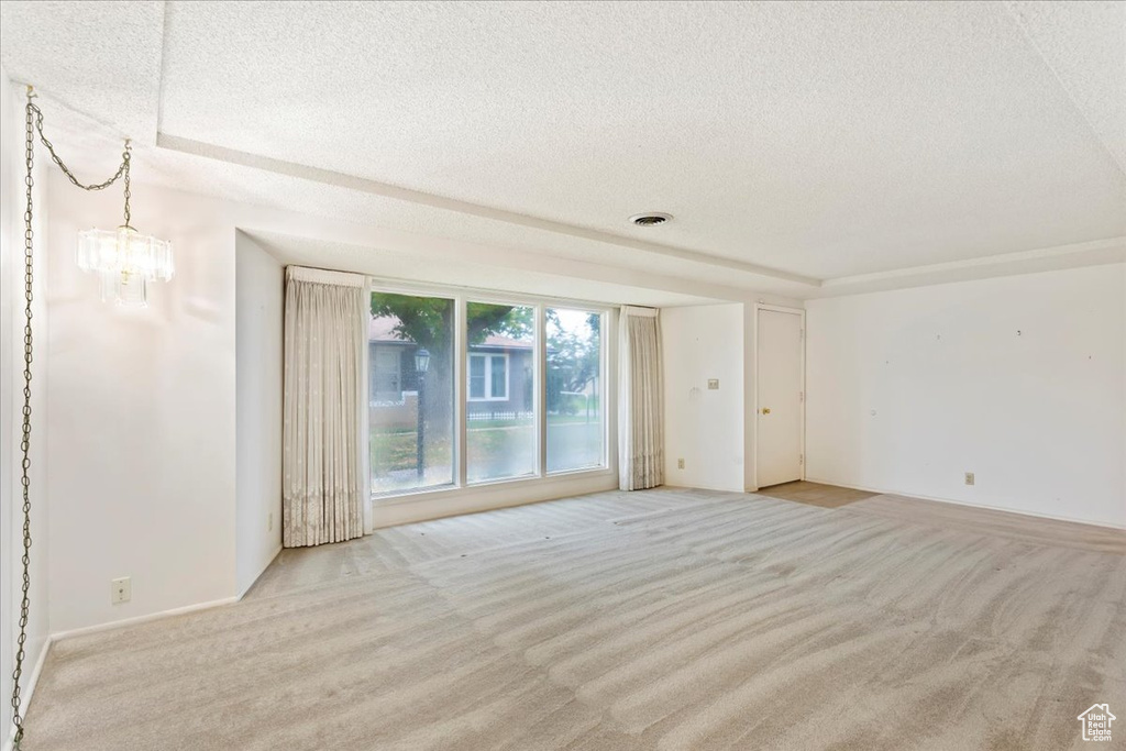 Empty room with an inviting chandelier, a textured ceiling, and light colored carpet