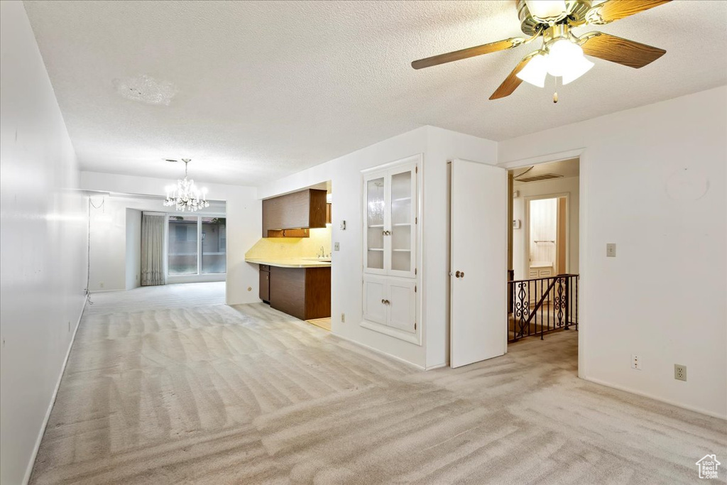 Unfurnished living room featuring light carpet, a textured ceiling, and ceiling fan with notable chandelier