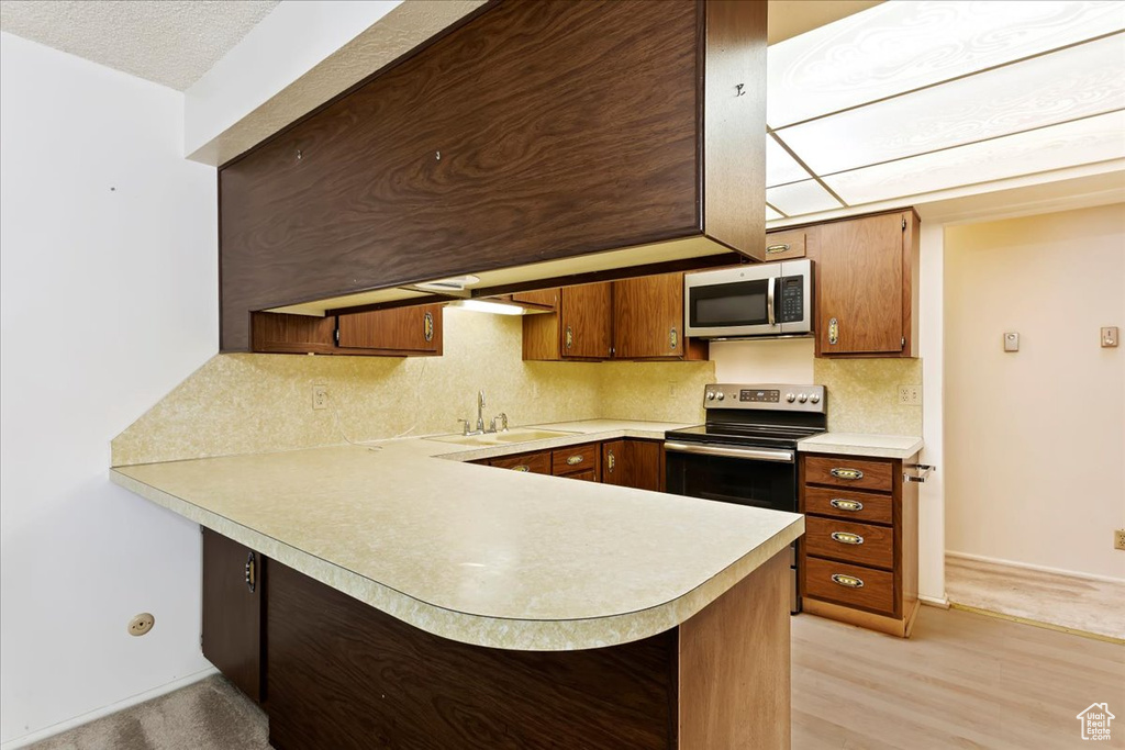 Kitchen with kitchen peninsula, stainless steel appliances, sink, light hardwood / wood-style floors, and tasteful backsplash