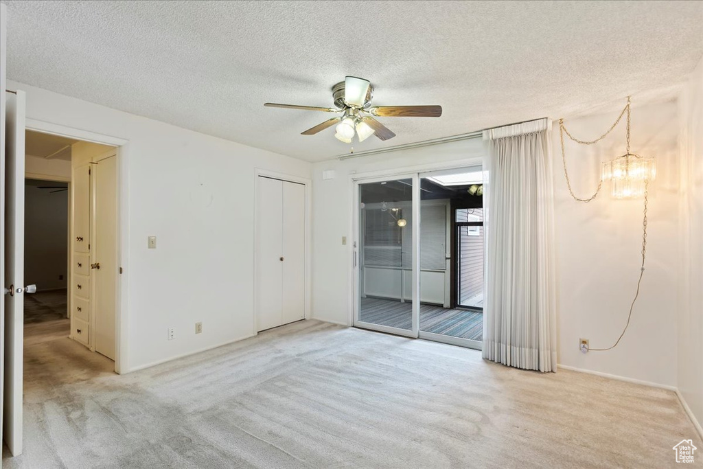 Carpeted empty room with a textured ceiling and ceiling fan with notable chandelier