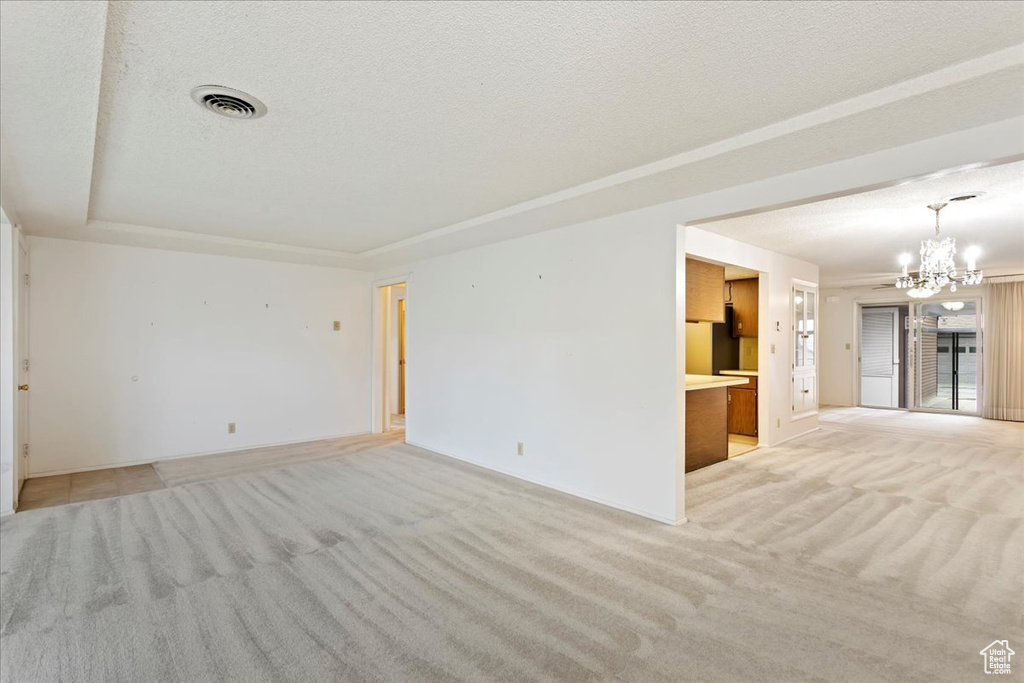 Unfurnished room with light carpet, a notable chandelier, and a textured ceiling