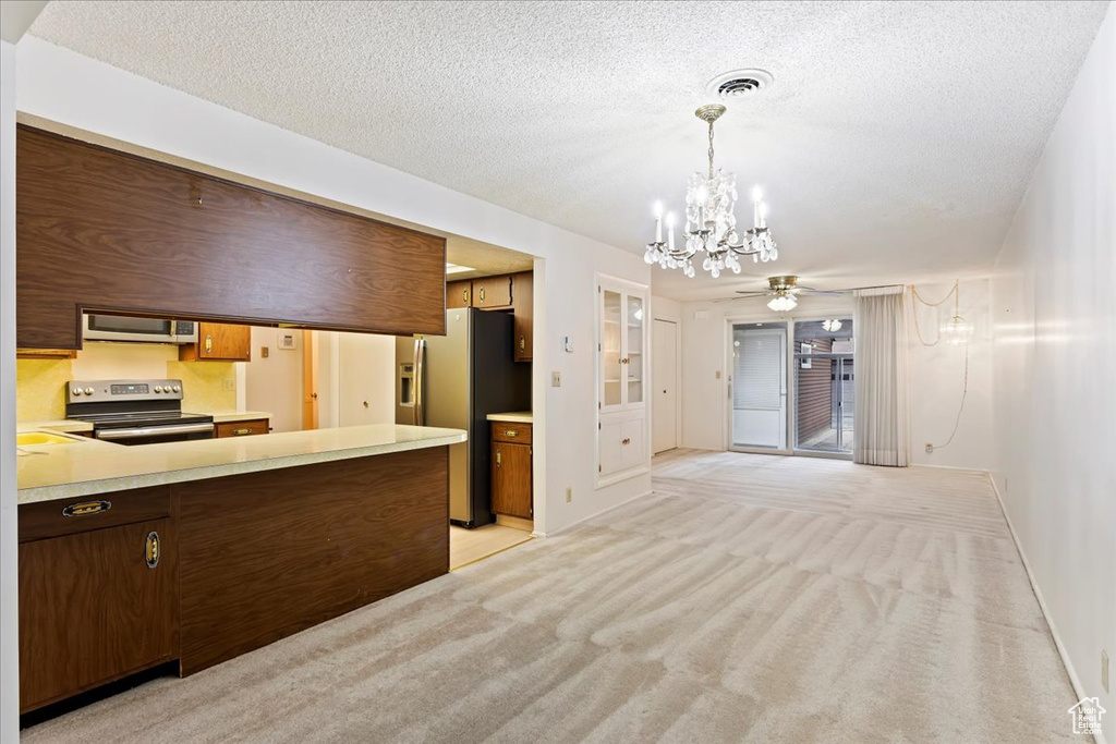 Kitchen with decorative light fixtures, stainless steel appliances, ceiling fan with notable chandelier, and light colored carpet