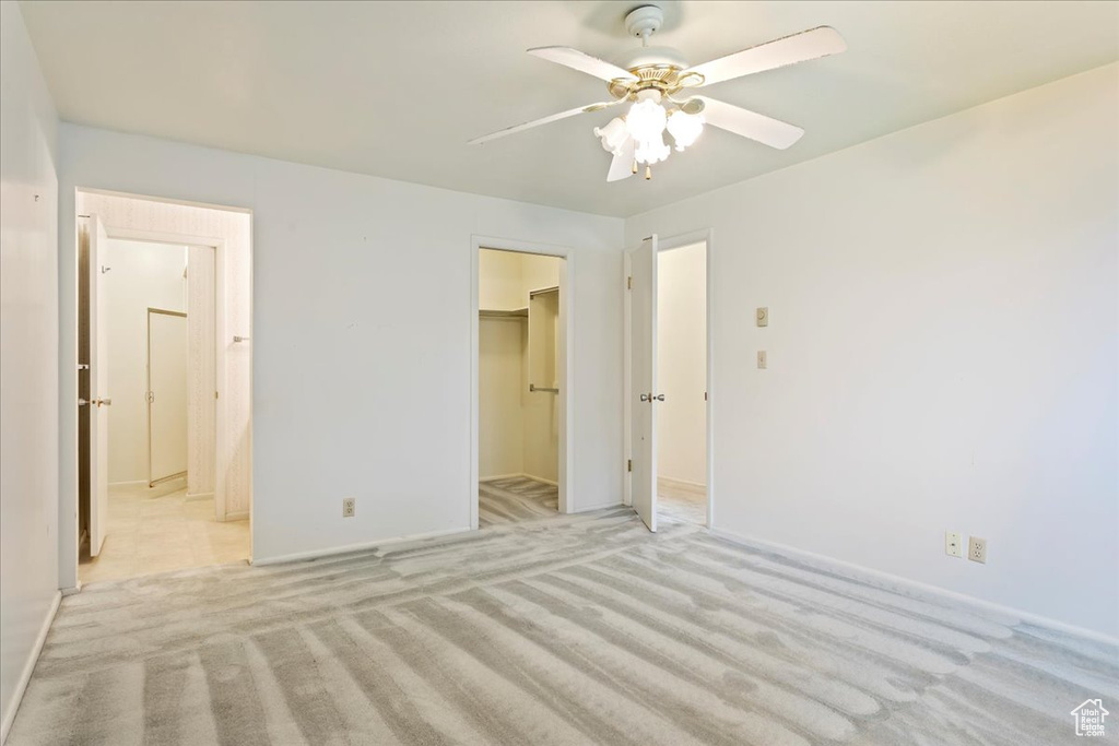 Unfurnished bedroom with a closet, ceiling fan, a walk in closet, and light colored carpet