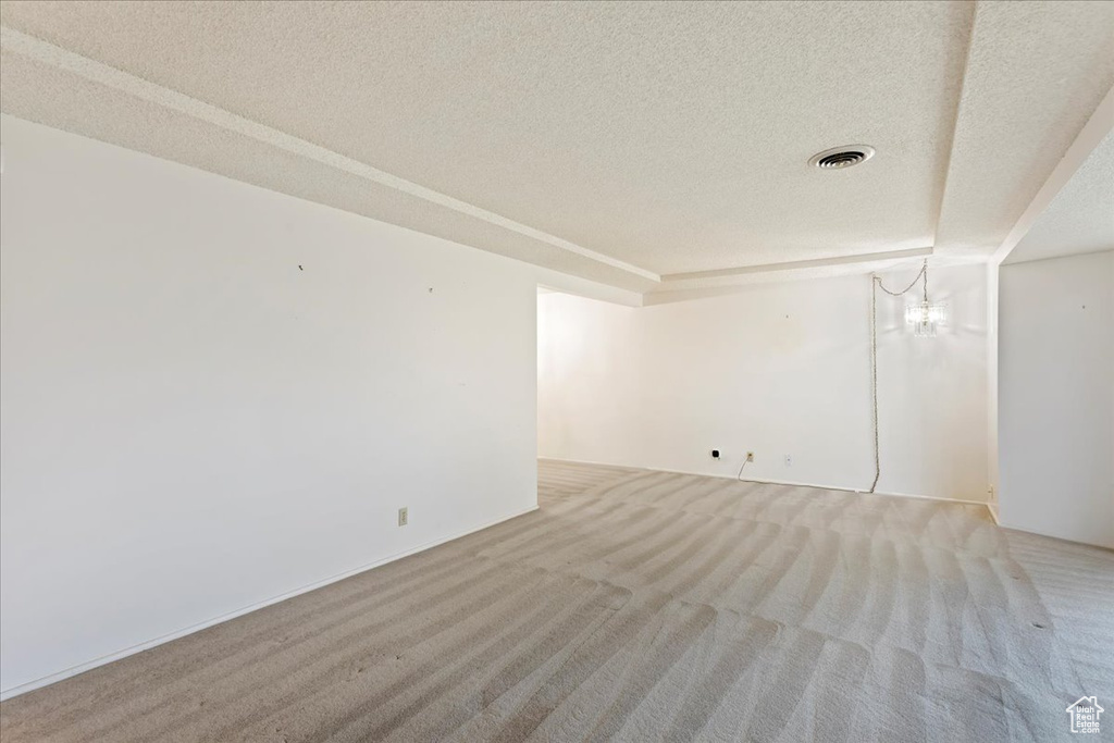 Empty room with a notable chandelier, a textured ceiling, and light colored carpet