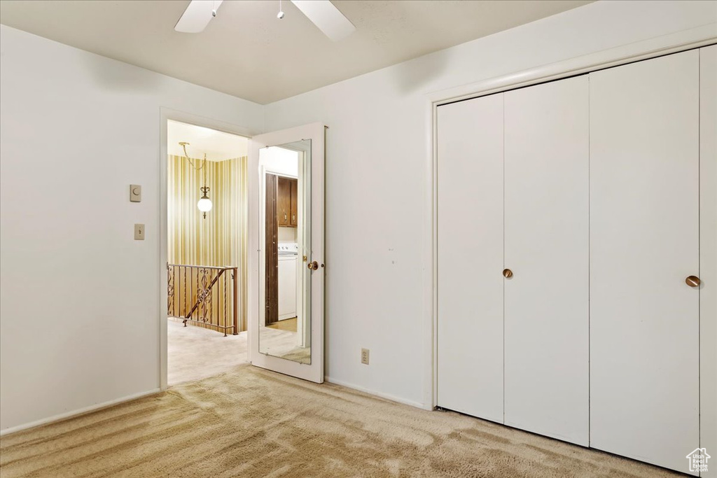 Unfurnished bedroom featuring light carpet, a closet, washer / dryer, and ceiling fan