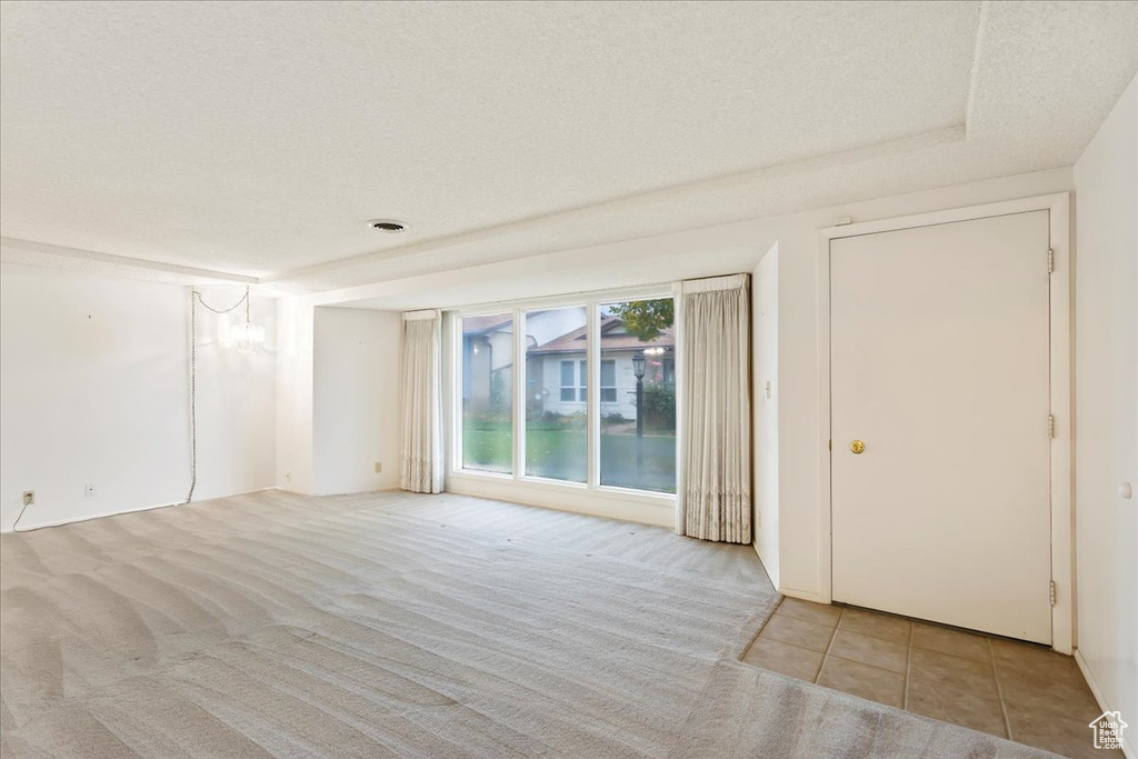 Carpeted empty room with a notable chandelier and a textured ceiling