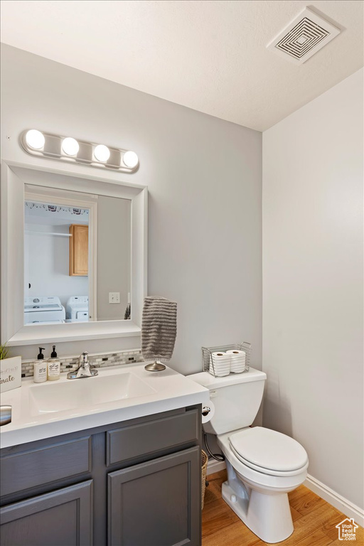 Bathroom featuring toilet, hardwood / wood-style floors, vanity, and washing machine and dryer