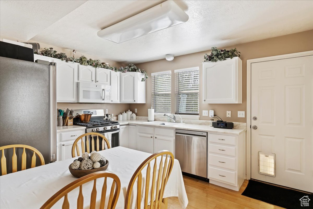 Kitchen with white cabinetry, stainless steel appliances, light hardwood / wood-style flooring, and sink