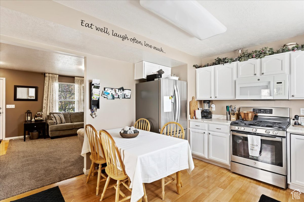 Kitchen with appliances with stainless steel finishes, light hardwood / wood-style flooring, white cabinets, and a textured ceiling