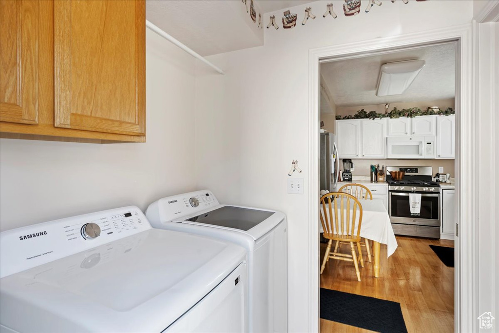 Clothes washing area featuring independent washer and dryer, light wood-type flooring, and cabinets