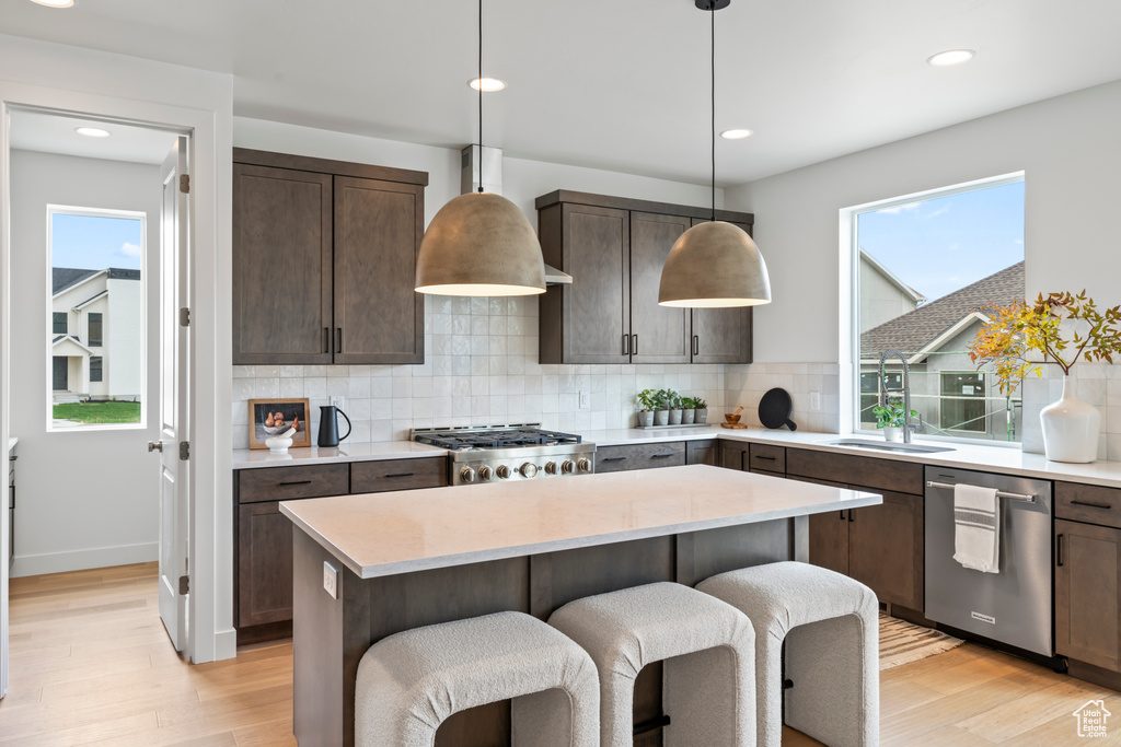 Kitchen featuring light hardwood / wood-style floors, pendant lighting, dark brown cabinetry, decorative backsplash, and appliances with stainless steel finishes