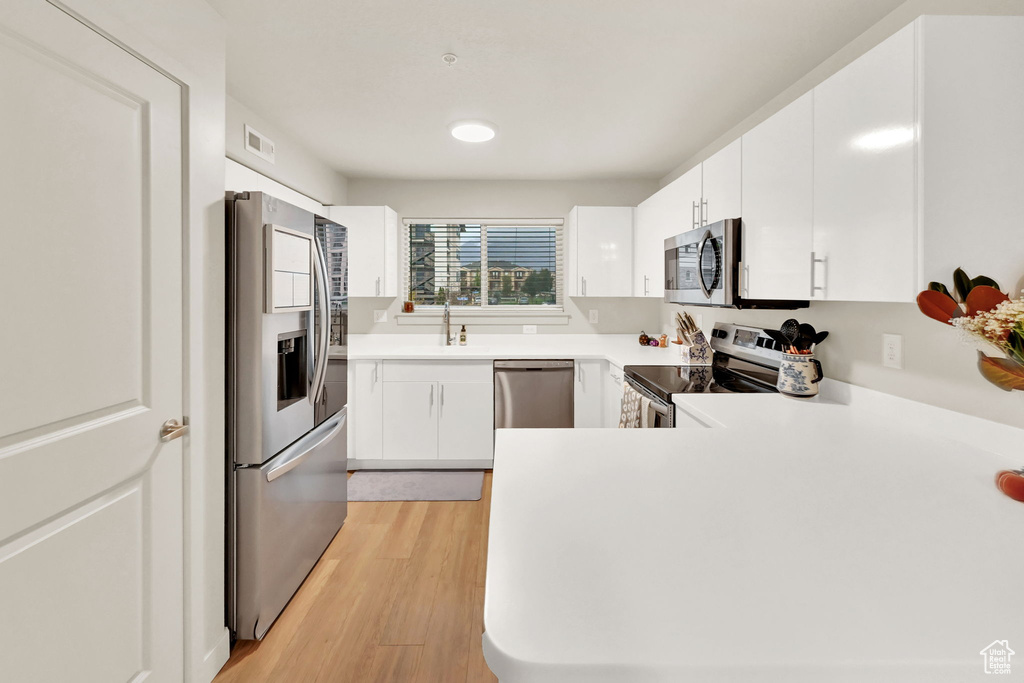 Kitchen featuring light hardwood / wood-style flooring, kitchen peninsula, stainless steel appliances, sink, and white cabinets