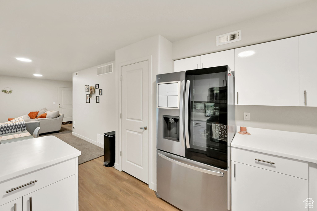 Kitchen with white cabinets, light wood-type flooring, and stainless steel refrigerator with ice dispenser