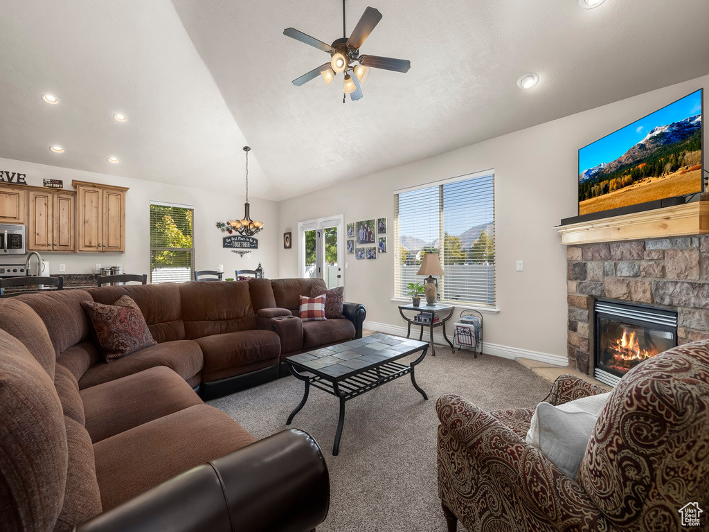 Carpeted living room with lofted ceiling, ceiling fan, and a stone fireplace