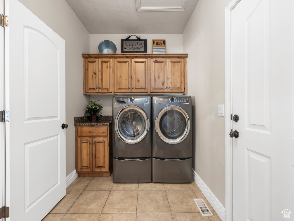 Laundry room with cabinets, washer and dryer, and light tile patterned flooring