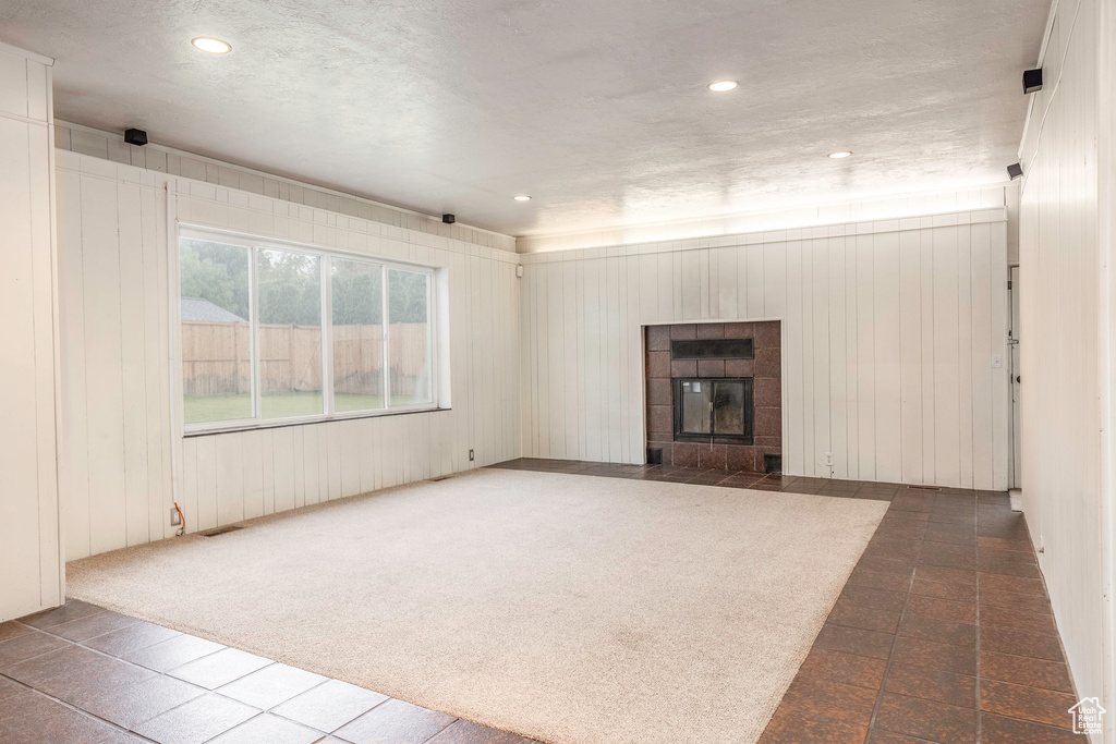 Unfurnished living room featuring dark colored carpet, a fireplace, and wood walls