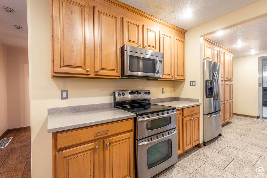 Kitchen with appliances with stainless steel finishes, a textured ceiling, and light wood-type flooring