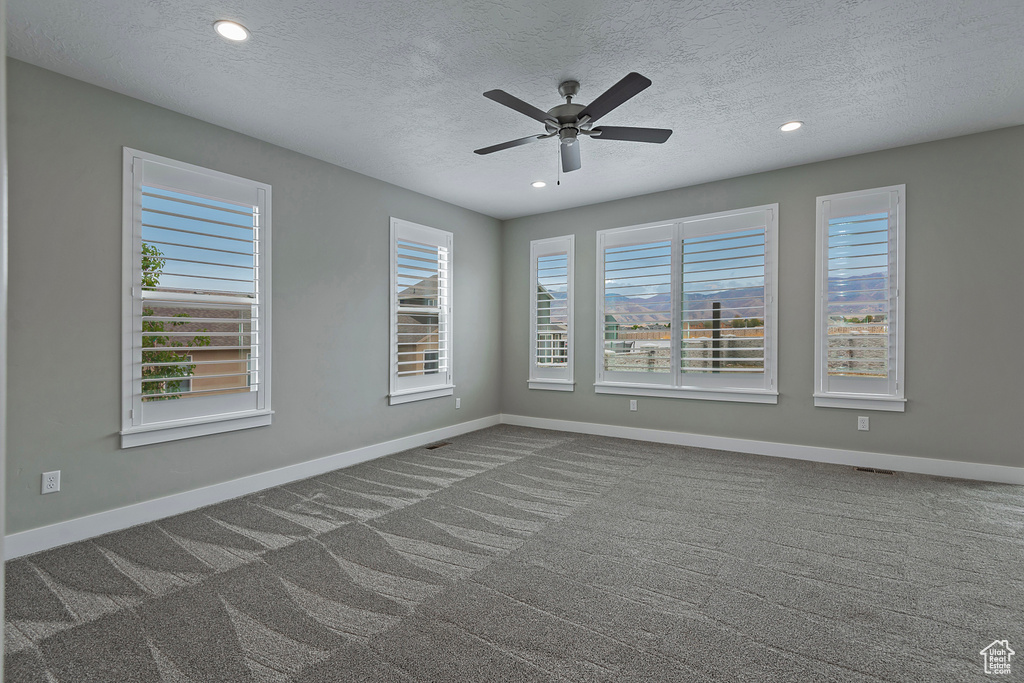 Carpeted empty room featuring a textured ceiling and ceiling fan