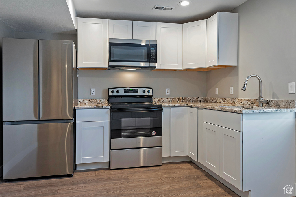 Kitchen featuring light hardwood / wood-style flooring, white cabinetry, and stainless steel appliances