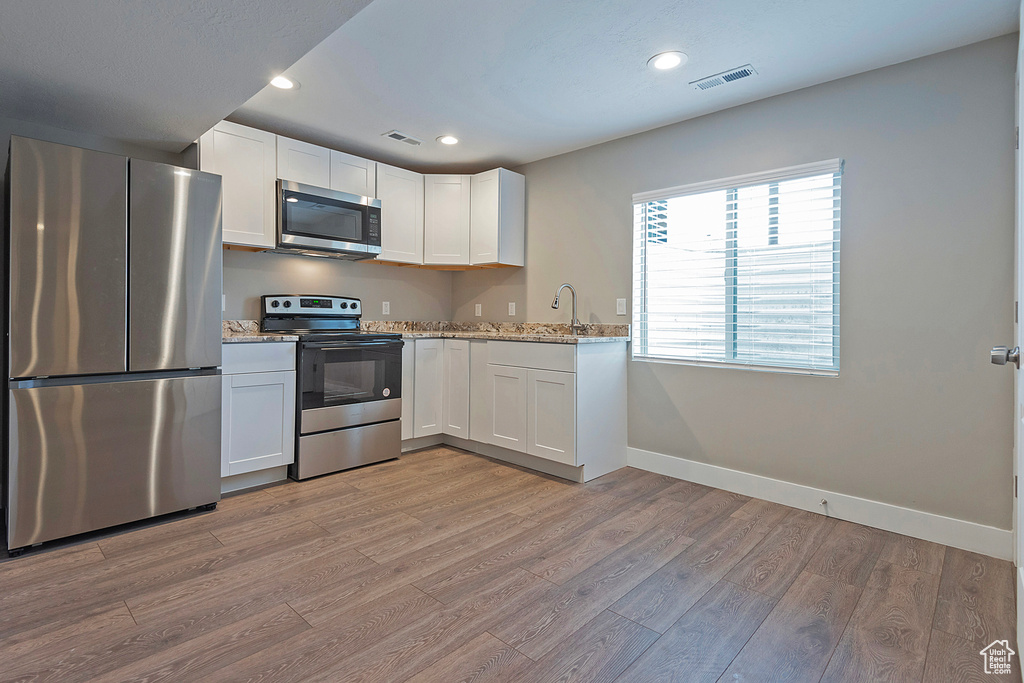 Kitchen featuring sink, white cabinetry, appliances with stainless steel finishes, light stone counters, and light hardwood / wood-style floors