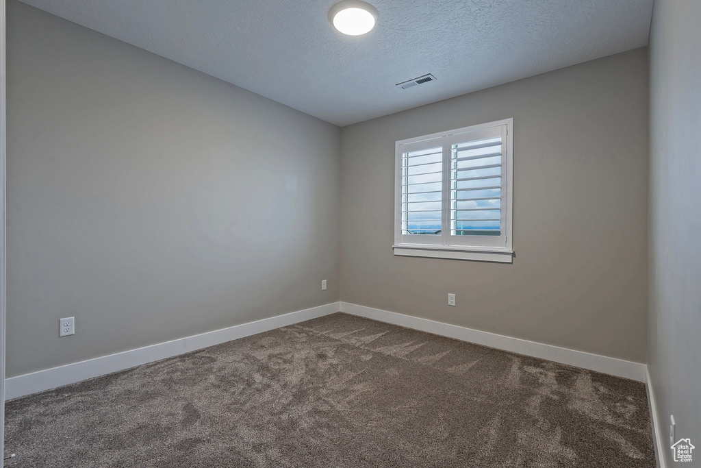 Spare room with a textured ceiling and dark colored carpet