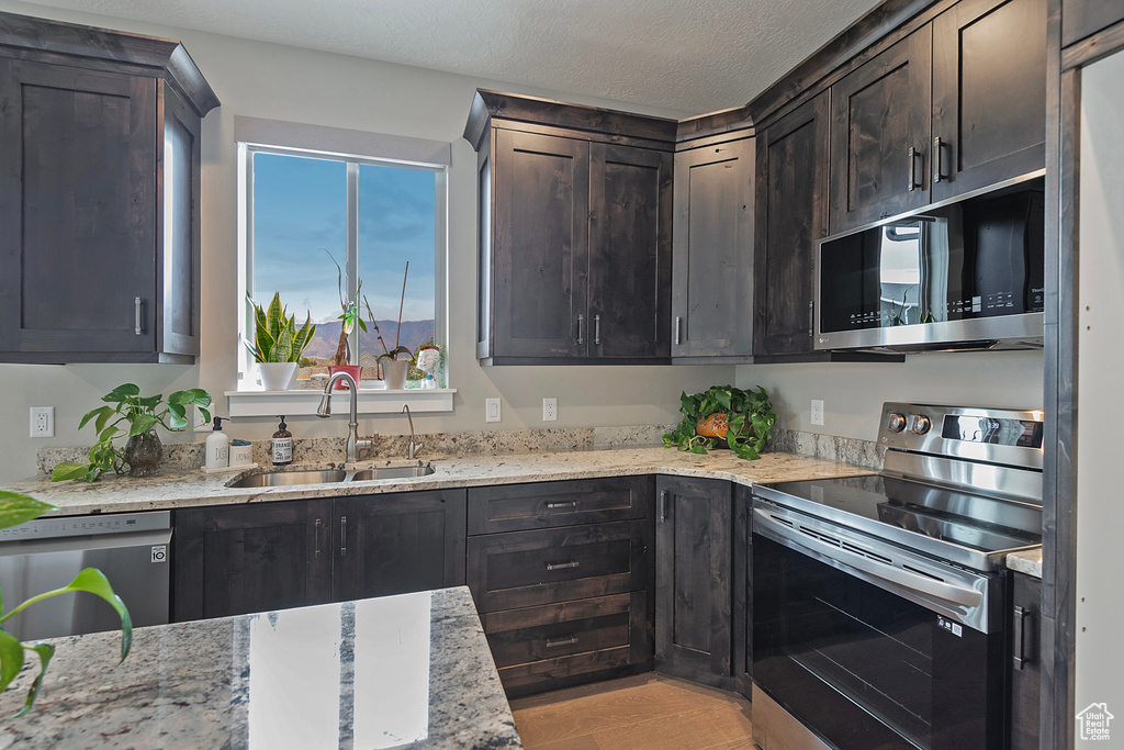 Kitchen with dark brown cabinets, sink, light stone countertops, appliances with stainless steel finishes, and a textured ceiling