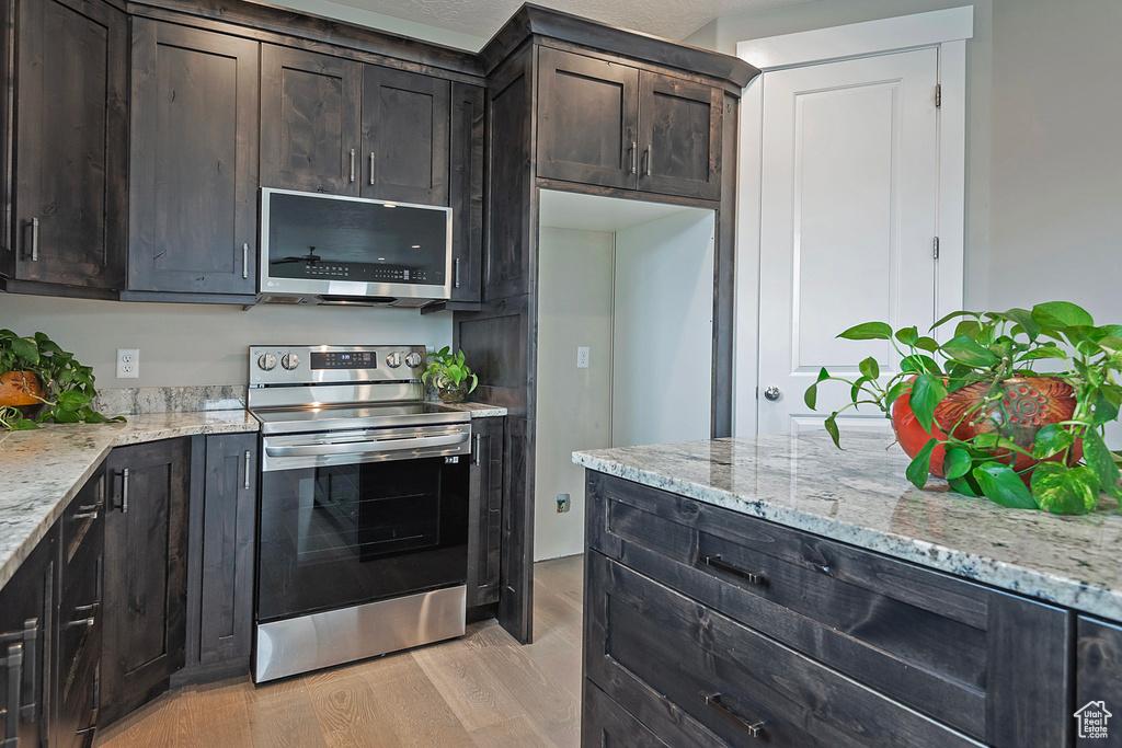 Kitchen featuring light stone counters, a textured ceiling, light hardwood / wood-style floors, dark brown cabinetry, and stainless steel appliances