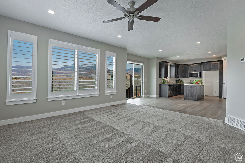 Unfurnished living room featuring light carpet, a textured ceiling, and ceiling fan