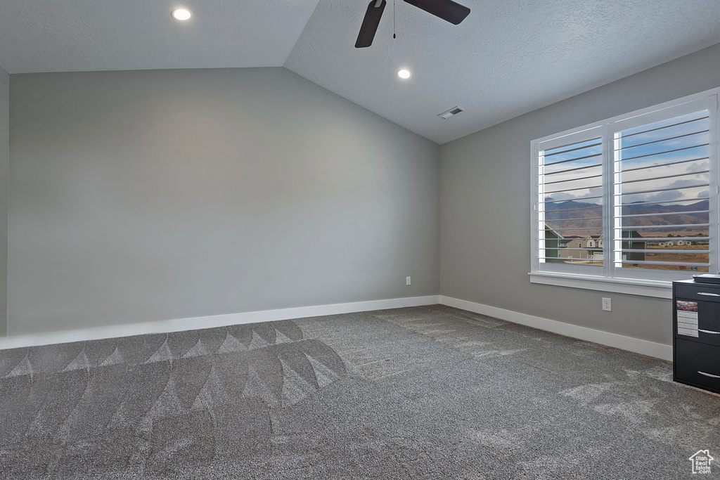 Empty room featuring a textured ceiling, ceiling fan, carpet flooring, and vaulted ceiling