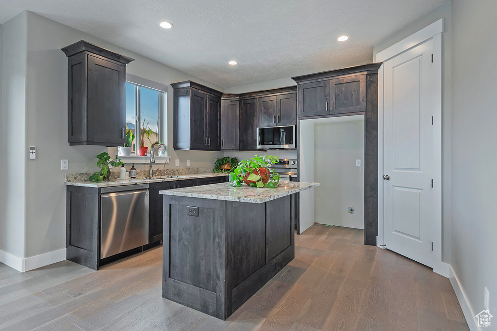 Kitchen with a kitchen island, light hardwood / wood-style flooring, dark brown cabinetry, appliances with stainless steel finishes, and light stone counters