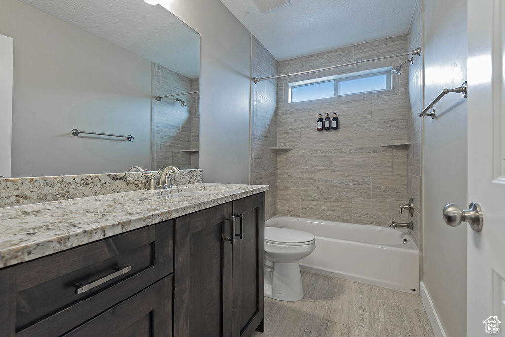 Full bathroom featuring tiled shower / bath, vanity, a textured ceiling, and toilet