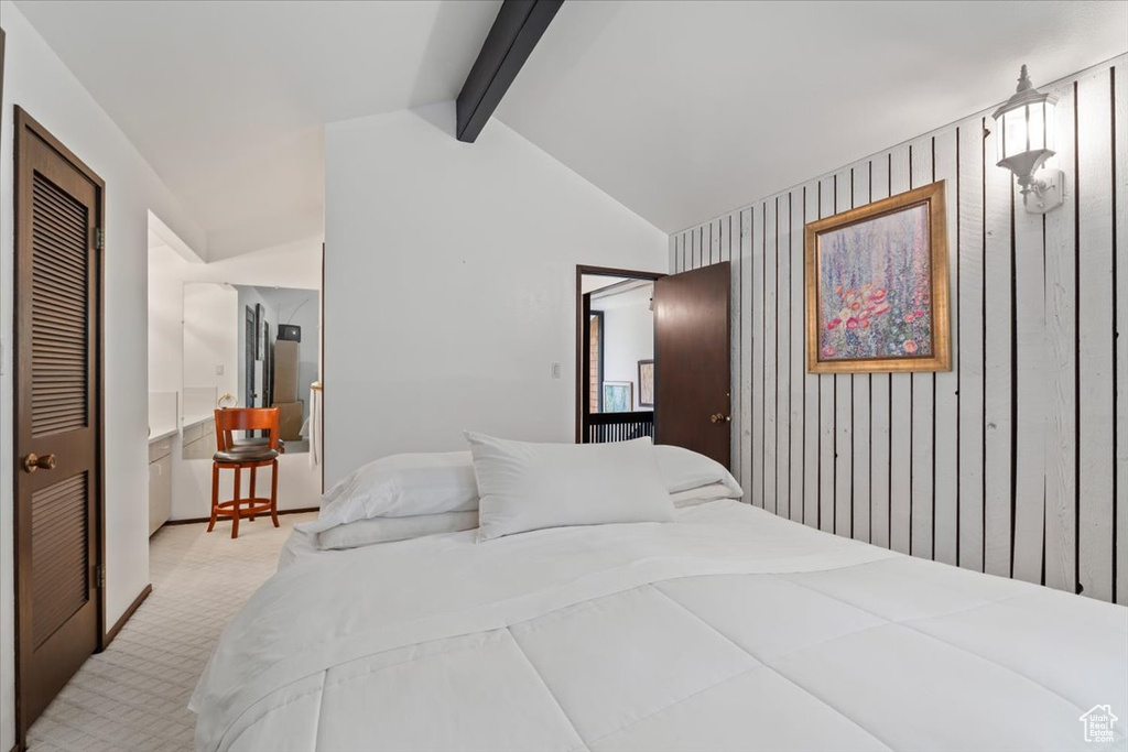 Carpeted bedroom featuring a closet, lofted ceiling with beams, and wooden walls