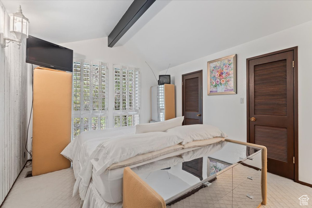 Bedroom with vaulted ceiling with beams and light carpet