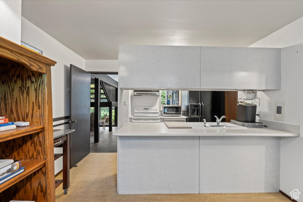 Kitchen with exhaust hood, black refrigerator with ice dispenser, white range oven, sink, and light colored carpet