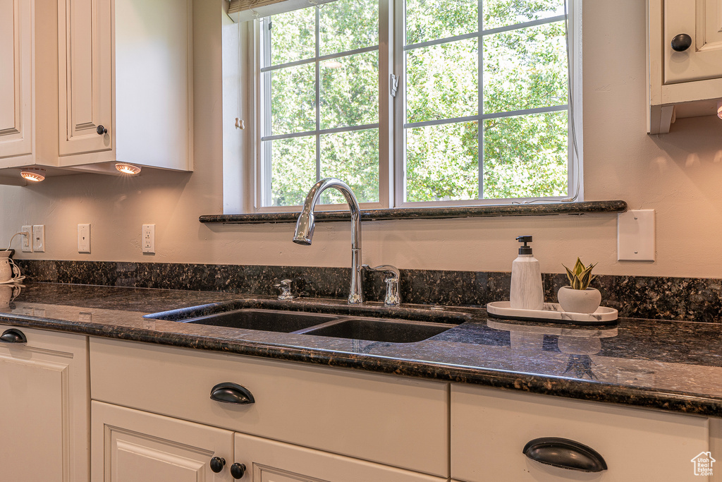 Kitchen featuring white cabinetry, sink, and dark stone counters